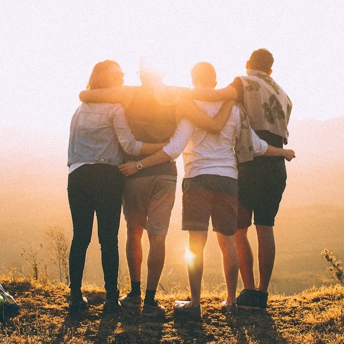 Friends embracing and facing sunrise