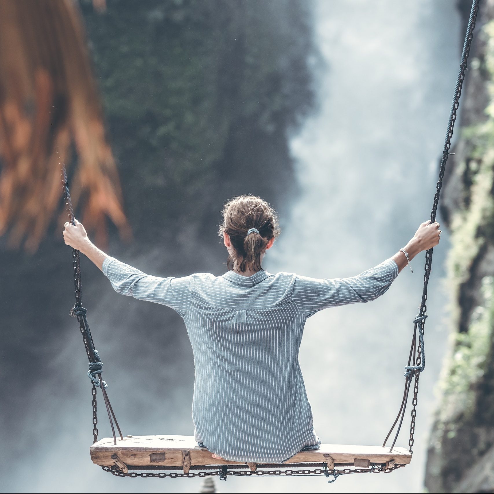 Woman sitting on a wooden, large swing in front of a waterfall